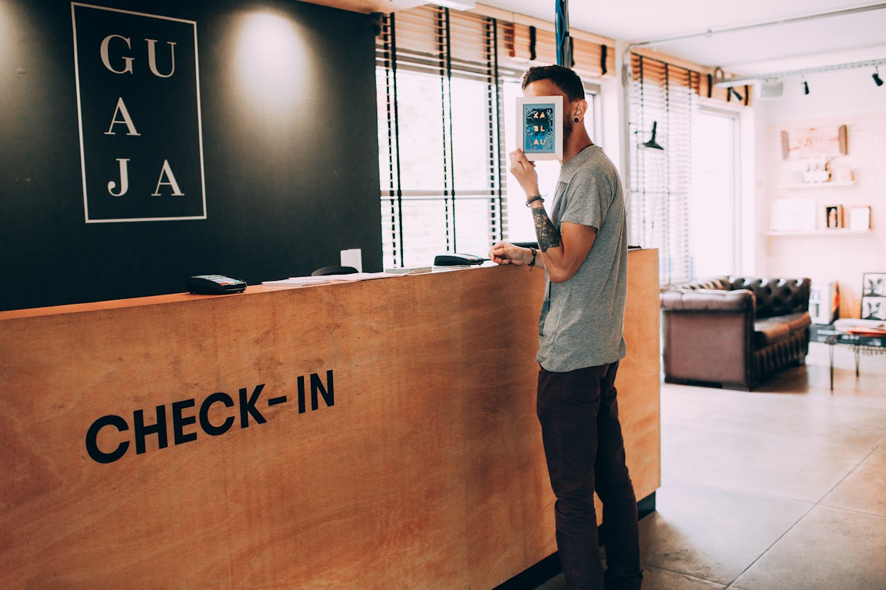 Man standing at a reception desk, holding a book, in a modern hotel lobby.